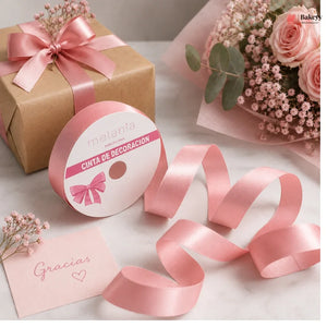 Pink ribbon with decorative packaging, flowers, and a card on a light surface