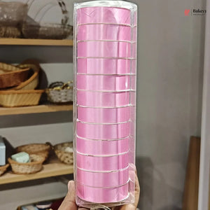 Roll of pink ribbon in clear packaging held in front of a shelf with wicker baskets.