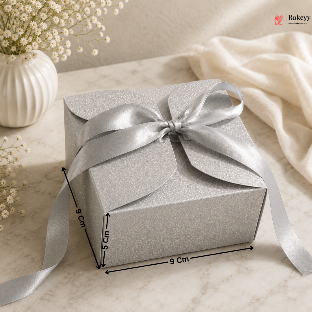 Silver gift box with a bow on a marble surface with decorative elements.