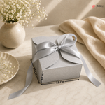 Silver gift box with a bow on a beige surface with flowers and a vase.