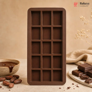 A rectangular chocolate mold with 15 dark brown cavities, styled on a beige surface with chocolate pieces, cocoa beans, and a bowl of chocolate sauce. The Bakeyy brand logo is visible in the top right corner.