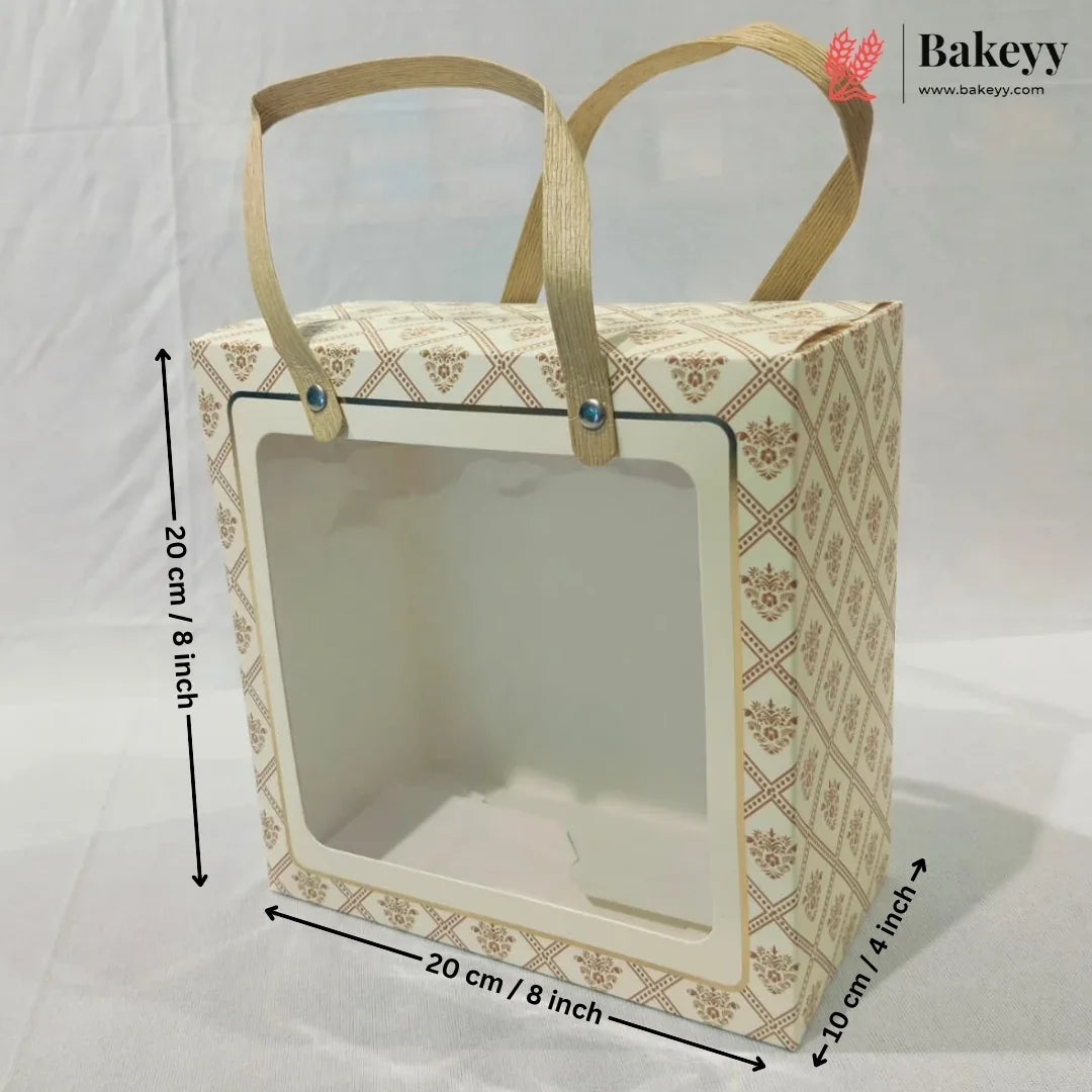 A rectangular bakery gift bag or display box with a clear front window and two tan handles, shown on a white backdrop with dimension arrows and labels indicating 20 cm by 20 cm by 10 cm.
