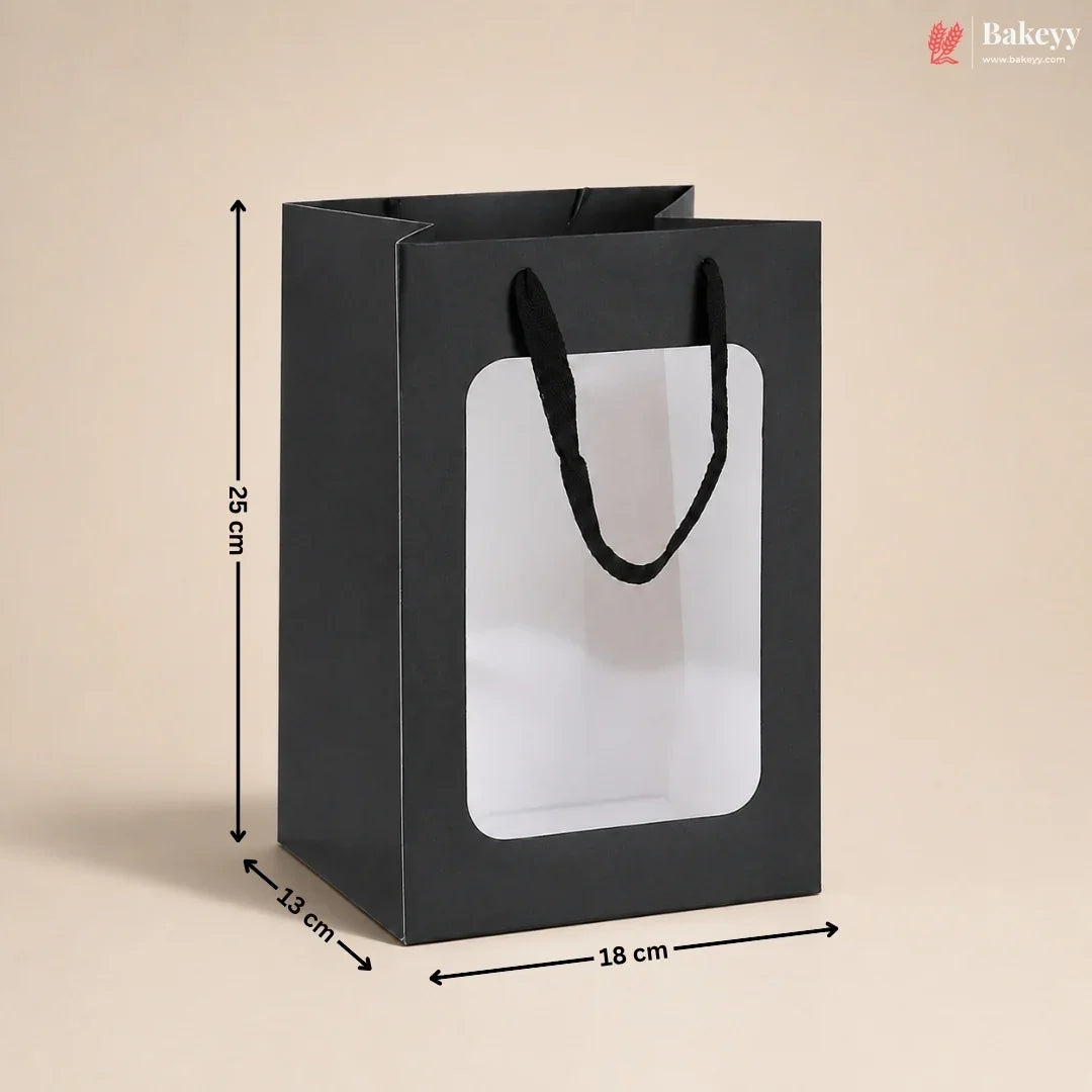 A black paper gift bag with black handles and a large clear front window, shown with dimension arrows and labels indicating 25 cm height, 13 cm width, and 18 cm depth on a beige background.