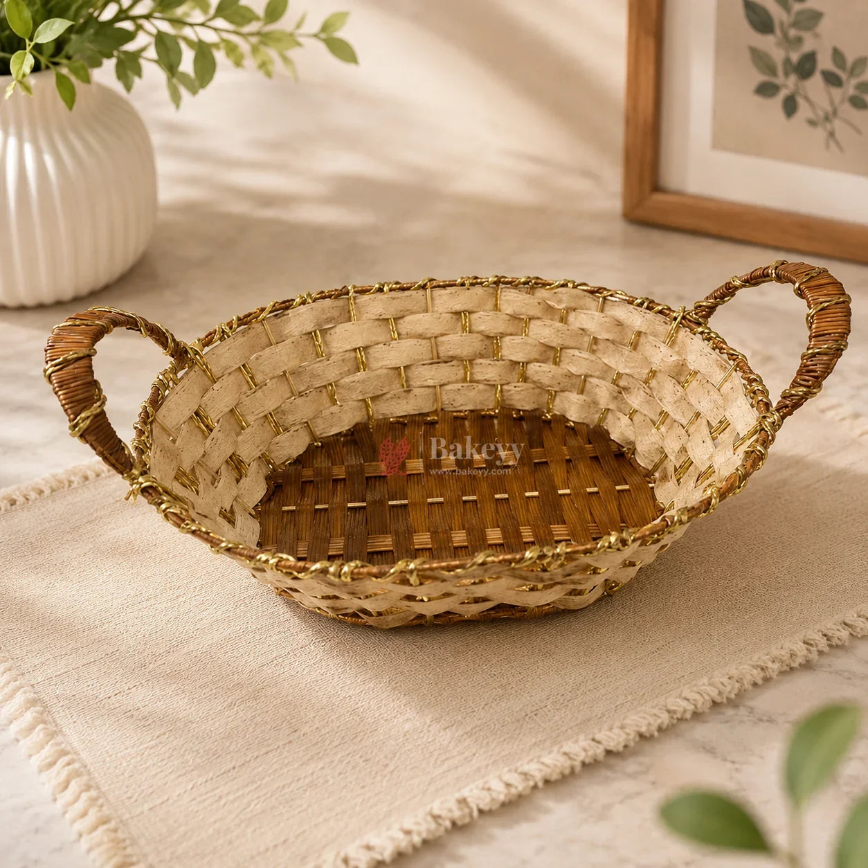 Woven bread basket with handles on a light surface, surrounded by plants.