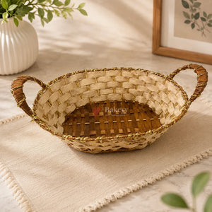 Woven bread basket with handles on a light surface, surrounded by plants.
