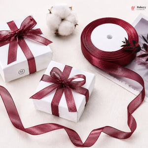 Two white gift boxes with red ribbons on a light surface, with a roll of red ribbon and cotton flowers in the background.