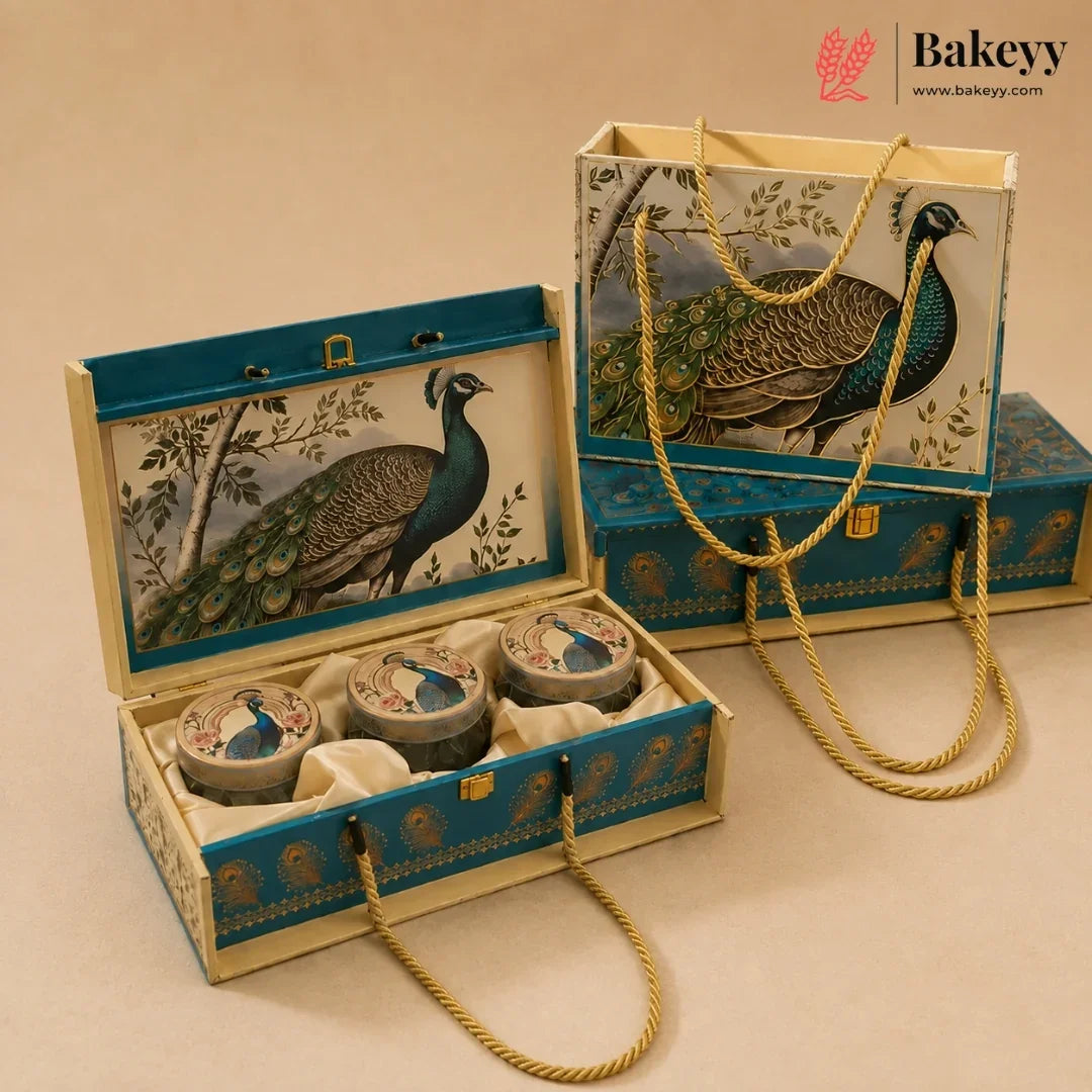 A decorative gift box set for baked goods, featuring an open rectangular box with three round tin containers inside, alongside a matching tote bag and closed box. The packaging is decorated with a detailed peacock illustration and blue-gold patterns on a cream background, with gold rope handles.