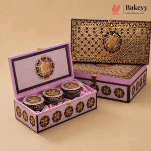 An ornate rectangular gift box set with three small round jars inside, shown open and closed on a warm beige background. The packaging features intricate gold, black, and purple floral patterns, and the Bakeey brand logo is visible in the top right corner.