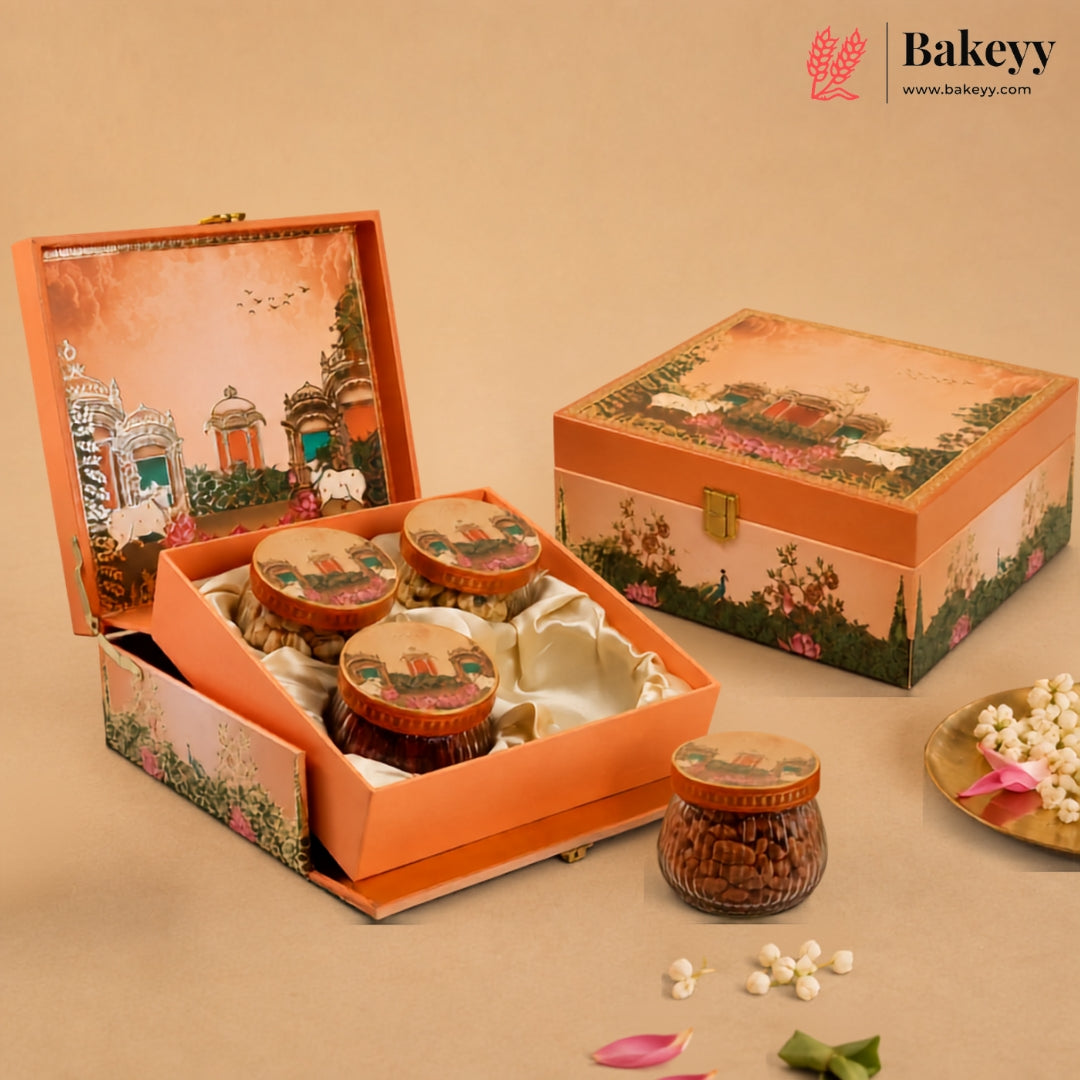 An orange decorative gift box set from Bakeyy, featuring an open box with three jars of sweets and a closed matching box on a beige background with decorative flower petals.