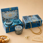 An ornate blue gift set box with gold detailing, shown open and closed on a beige background. The set includes decorative glass jars with blue lids, a blue satin lining, a gold rope handle, and a small card reading 'For Your Special Moments.