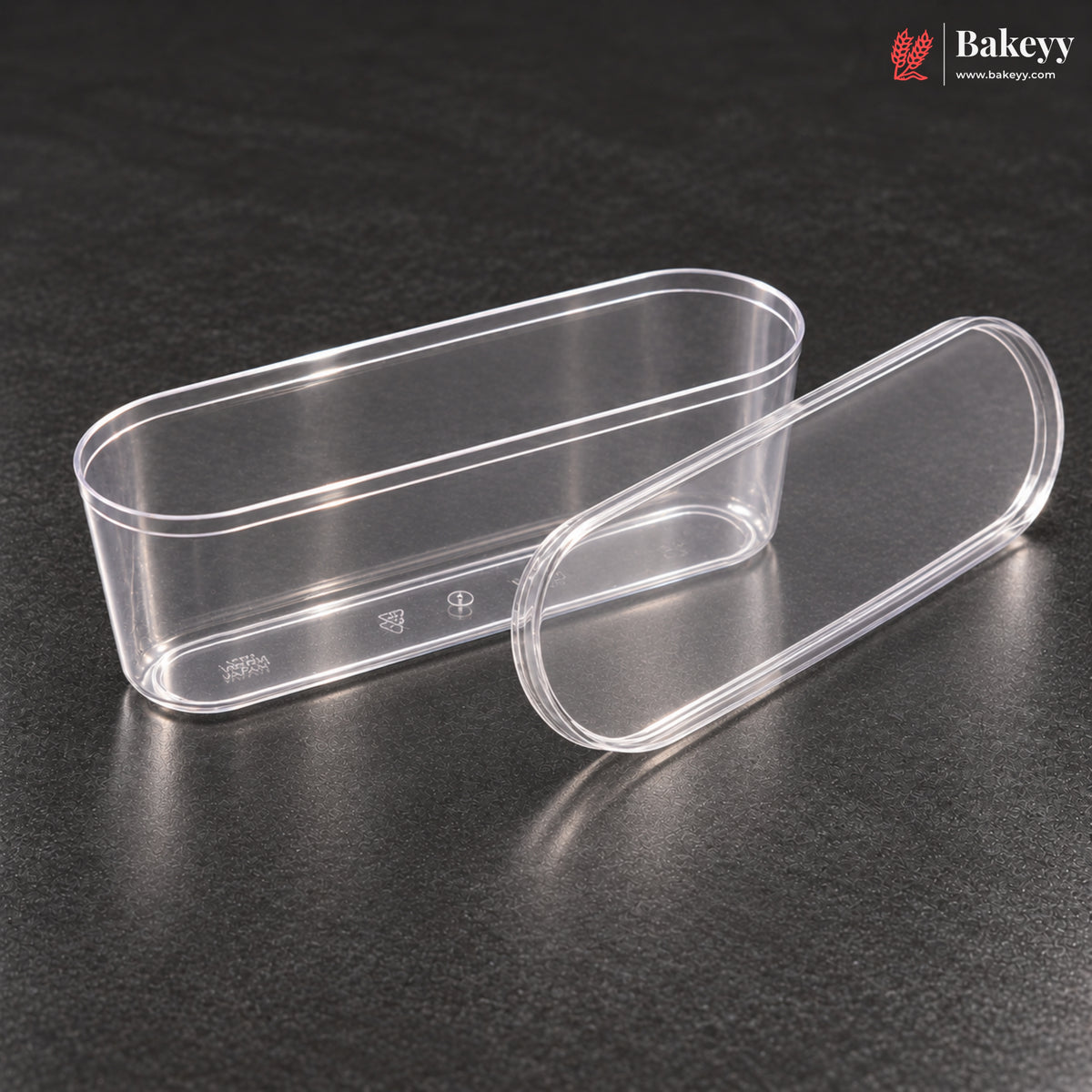 Two clear plastic oval containers, one rectangular with a lid and one rounded capsule-shaped with its lid, displayed on a dark textured surface. The Bakeey brand logo is visible in the top right corner.