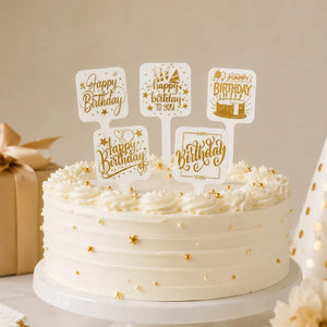 White cake with gold decorations and 'Happy Birthday' topper on a neutral background