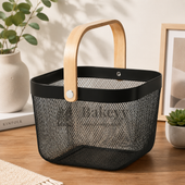 Black mesh basket with wooden handle on a wooden surface, surrounded by plants and books.