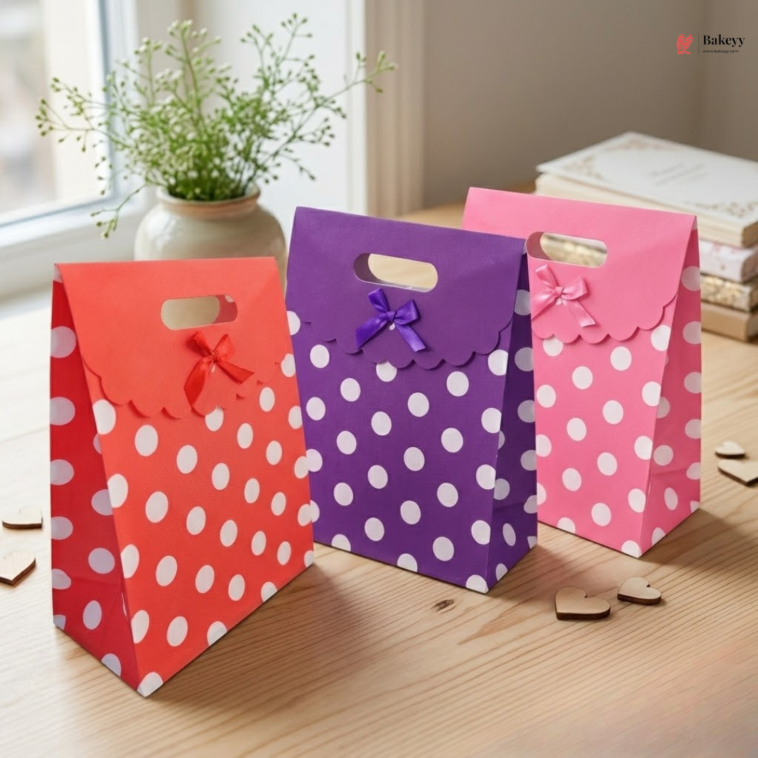 Three polka dot gift bags in red, purple, and pink on a wooden surface.