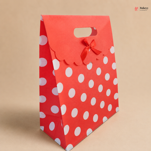 Red gift bag with white polka dots and a red ribbon on a beige background