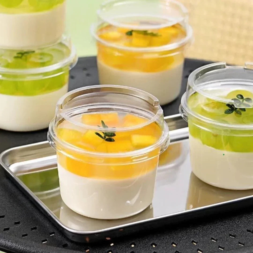 Small containers of layered dessert with white cream, yellow fruit, and green jelly on a metal tray.