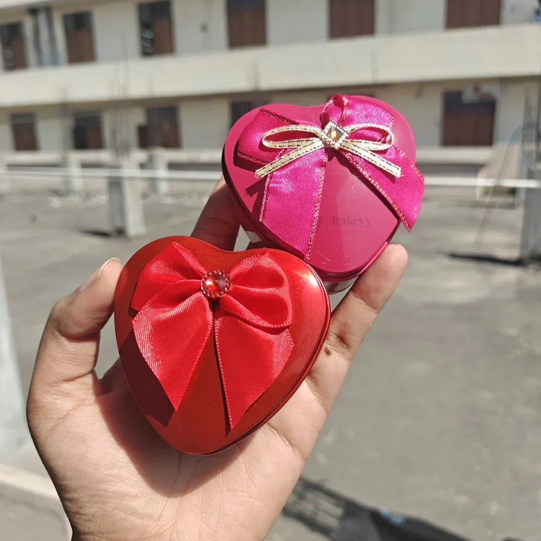 Hand holding two heart-shaped gift boxes with red and pink bows from Bakeyy, bakery packaging supplies.