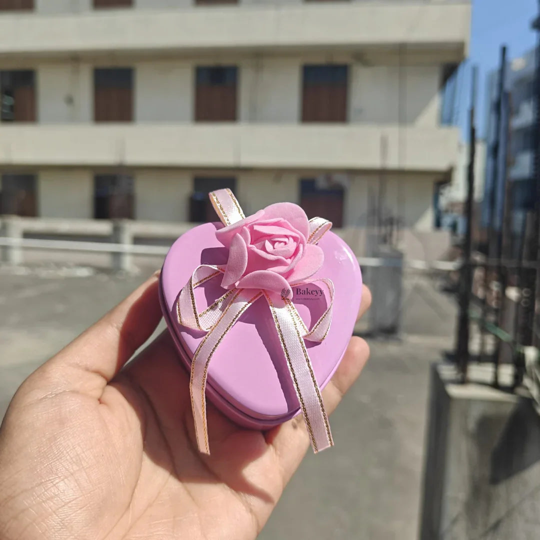 Hand holding a pink heart-shaped gift box with ribbon and rose from Bakeyy.com outdoors