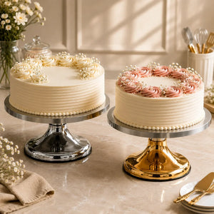 Two decorated cakes on stands with flowers and utensils in the background.