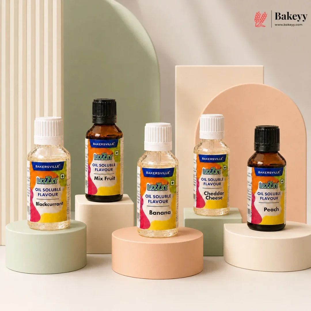 Four bottles of Bakeyville oil soluble flavours arranged on pastel display pedestals against a clean studio backdrop. The bottles include Makkurrim, Banana, Cheddar Cheese, and Peach flavours, with two amber glass bottles and two clear plastic bottles, each labeled with the Bakeyville logo.
