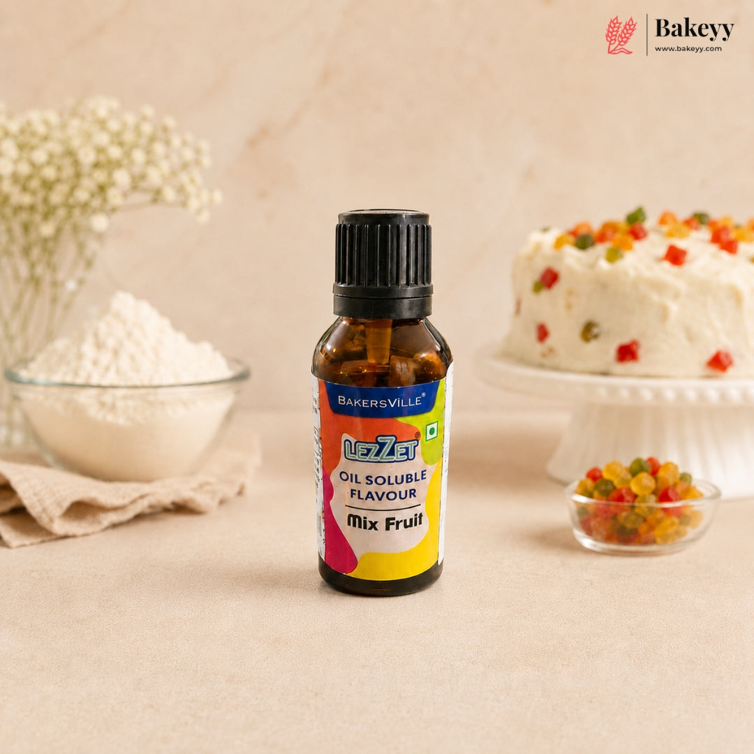 A bottle of Bakersville oil soluble flavouring mix, fruit flavour, standing on a beige surface with baking ingredients and a decorated cake blurred in the background.
