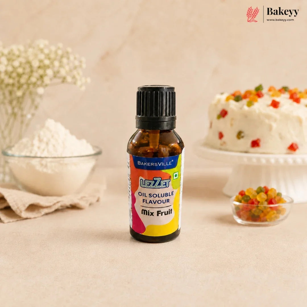 A bottle of Bakersville oil soluble flavouring mix, fruit flavour, standing on a beige surface with baking ingredients and a decorated cake blurred in the background.