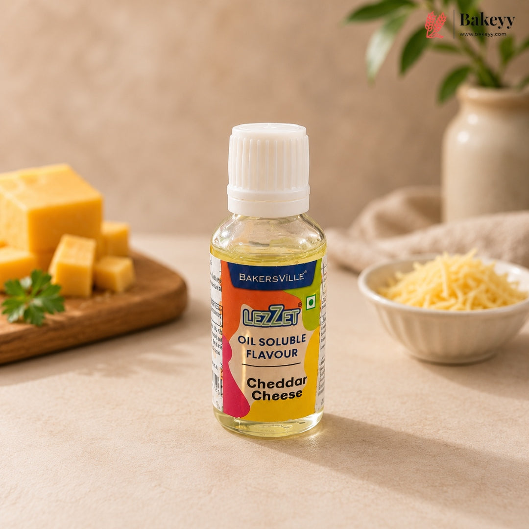 A bottle of Bakersville Liza Oil Soluble Flavour in Cheddar Cheese flavor, set on a beige surface with cheese props in the background.