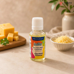 A bottle of Bakersville Liza Oil Soluble Flavour in Cheddar Cheese flavor, set on a beige surface with cheese props in the background.
