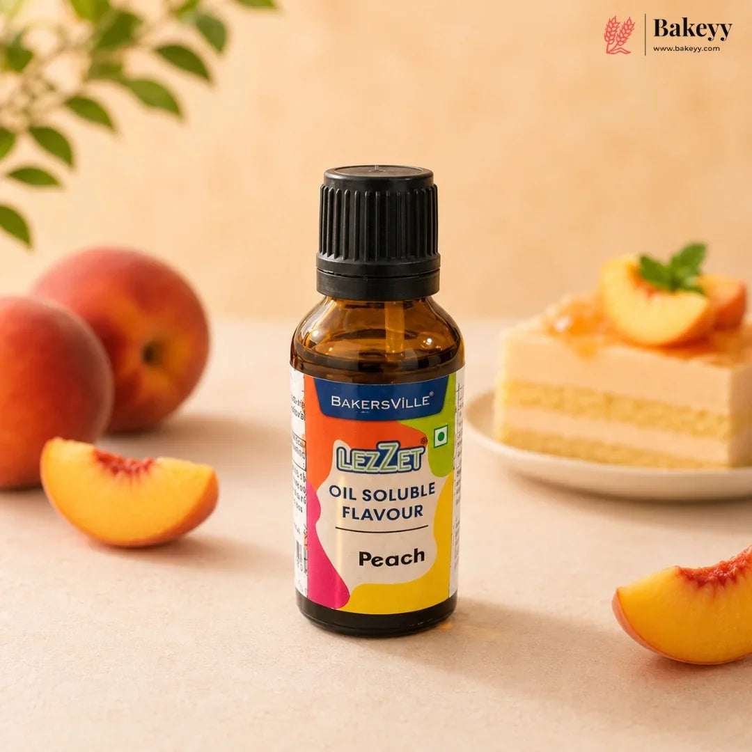 A bottle of BakersVille UzzZet Oil Soluble Flavour in Peach, shown in the foreground with fresh peach slices and a peach cake blurred in the background on a warm beige surface.
