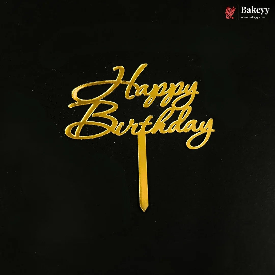 Gold metallic 'Happy Birthday' script cake topper on a black background, with a small Bakeyy logo in the top right corner.