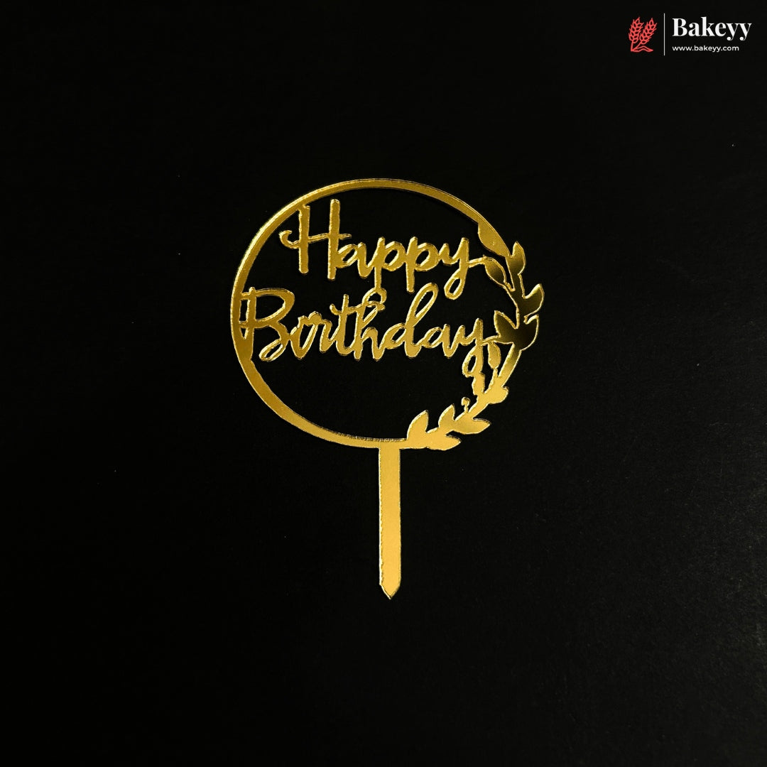 A gold metal 'Happy Birthday' cake topper with a laurel wreath design on a black background, featuring a Bakeyy brand watermark in the top right corner.