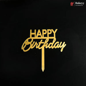 Gold metal 'HAPPY Birthday' cake topper with a vertical stick, displayed on a solid black background. A small 'Bakeyy' brand logo is visible in the top right corner.