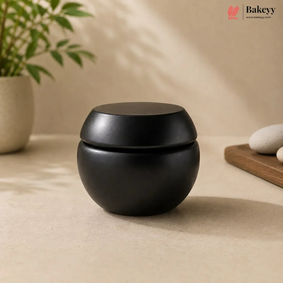 Black ceramic container on a beige surface with a plant and rocks in the background, featuring the Bakeyy brand.