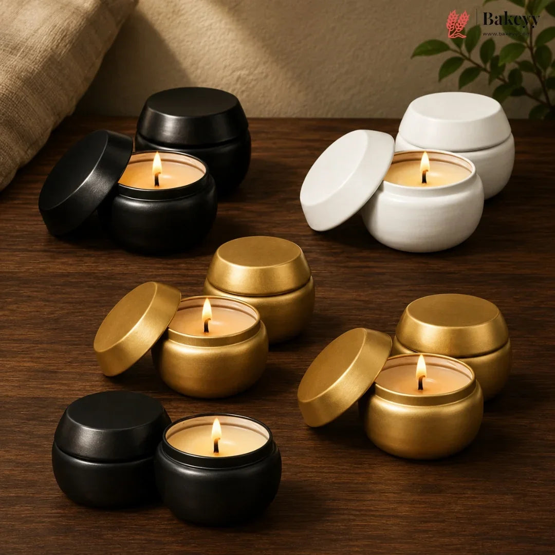 Various candles in black, gold, and white containers on a wooden surface.