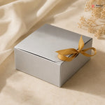 Silver gift box with a gold ribbon on a beige fabric background