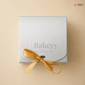 White gift box with a yellow ribbon on a beige background, featuring the Bakeyy brand.