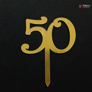 A gold metallic 50th birthday cake topper with a flat base stake, shown on a black background.