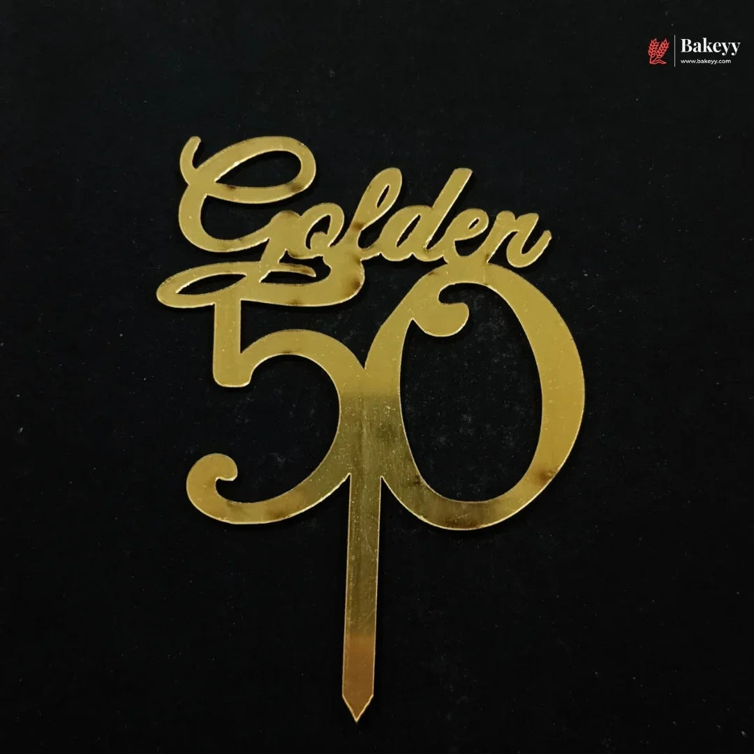 A gold metallic 'Golden 50' cake topper with a single wire stake, shown on a solid black background. A small 'Bakeyy' brand watermark is visible in the top right corner.