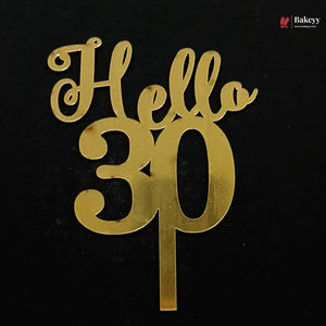 Gold metallic 'Hello 30' cake topper with a single stem, shown on a solid black background. A small 'Bakeyy' watermark is visible in the top right corner.