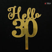 Gold metallic 'Hello 30' cake topper with a single stem, shown on a solid black background. A small 'Bakeyy' watermark is visible in the top right corner.