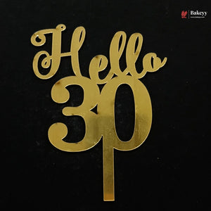 Gold metallic 'Hello 30' cake topper with a single stem, shown on a solid black background. A small 'Bakeyy' watermark is visible in the top right corner.