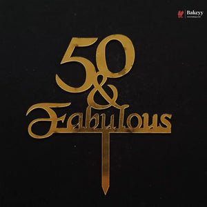 Gold metal cake topper with the text '50 & Fabulous' on a black background, featuring a small Bakeey watermark in the top right corner.