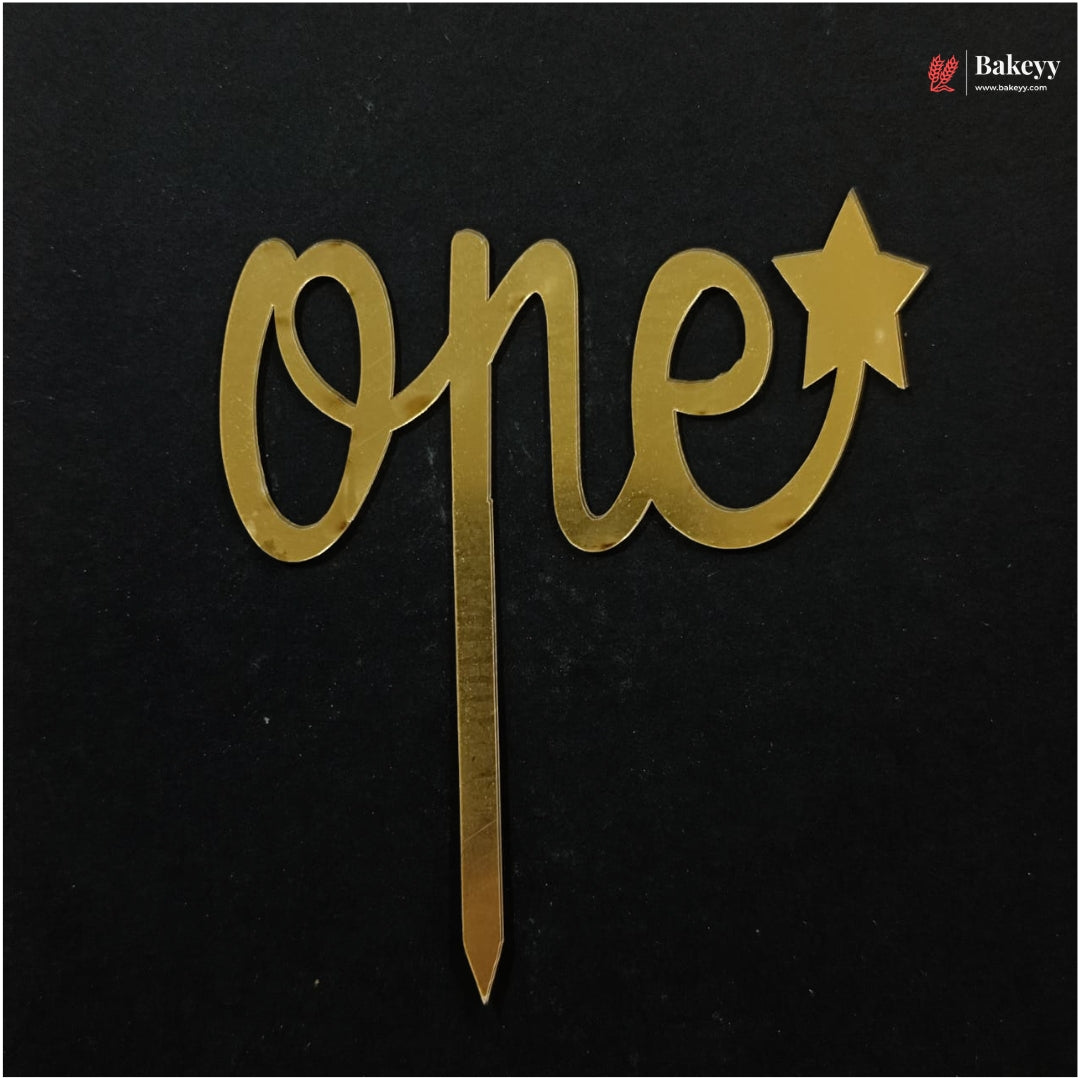 Gold metallic 'one' and star cake topper with a stick, displayed on a black background. A Bakeey brand logo is visible in the top right corner.
