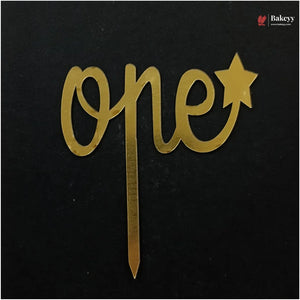 Gold metallic 'one' and star cake topper with a stick, displayed on a black background. A Bakeey brand logo is visible in the top right corner.