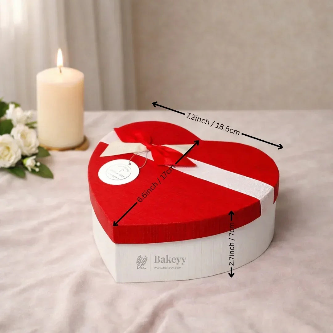 Heart-shaped red and white gift box with ribbon, Bakeyy.com, on table with candle and flowers