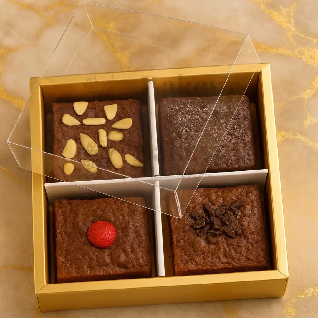 Four brownies in a gold box with a clear lid on a marble surface