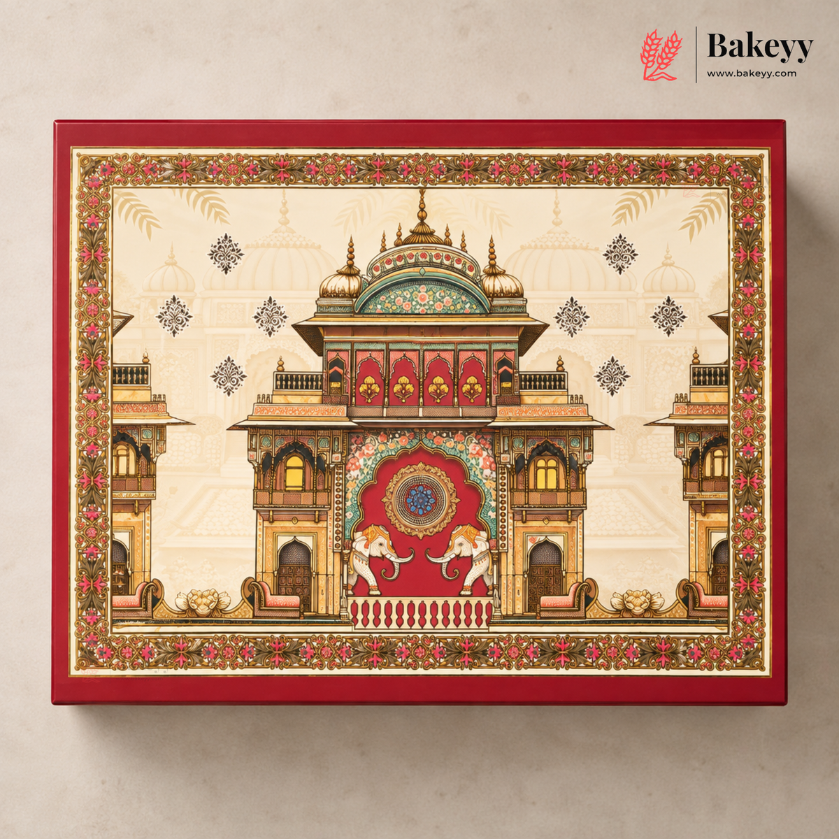 A rectangular red gift box with an ornate traditional palace illustration on the lid, photographed against a light beige wall. The Bakeyy logo appears in the top right corner.
