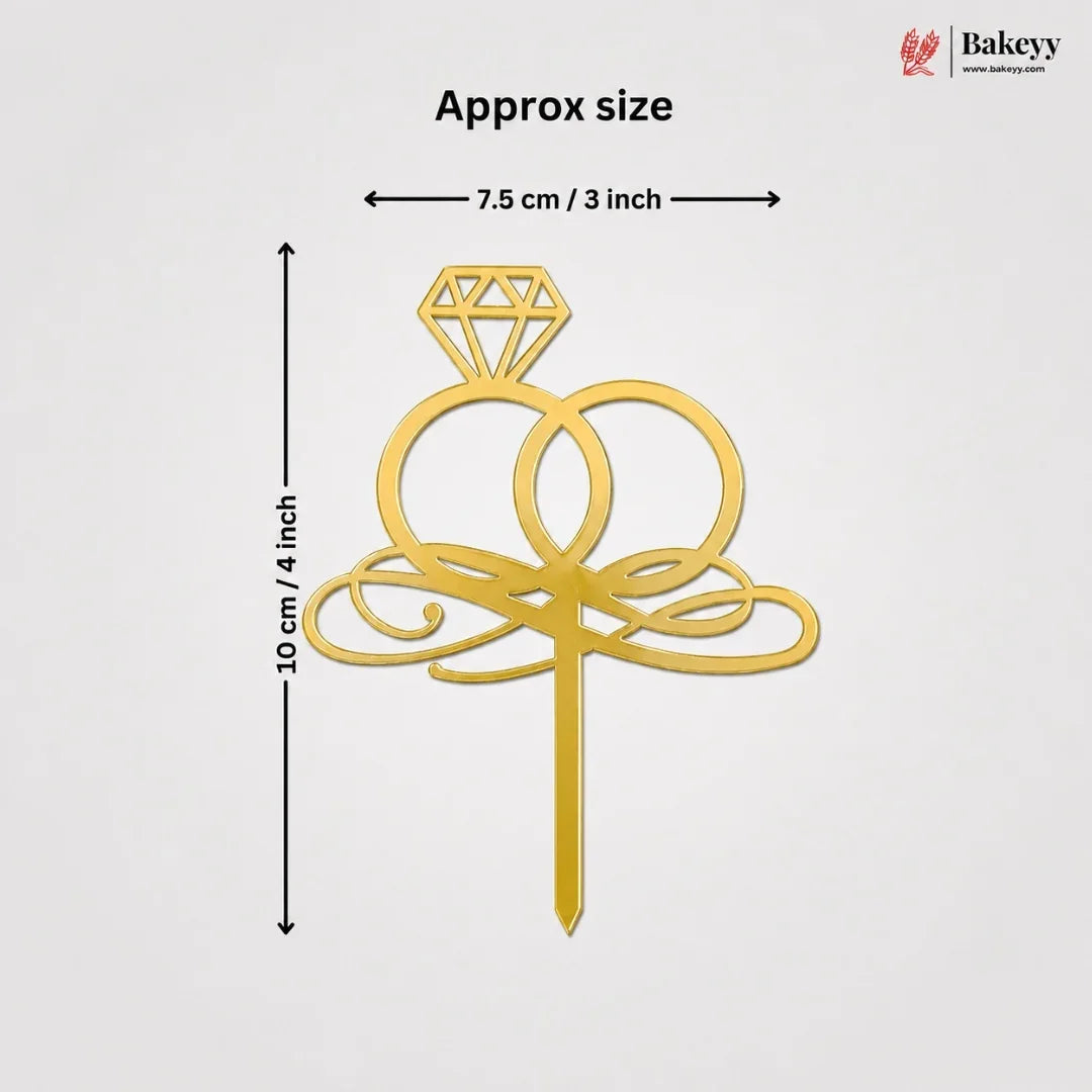 Gold ring cake topper with a diamond design and decorative scrollwork, shown with dimension lines indicating approximate size of 10 cm by 7.5 cm on a light gray background.