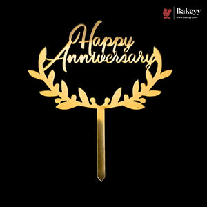 Gold laser-cut acrylic cake topper with 'Happy Anniversary' script and leafy wreath design on a black background, with a Bakeyy logo in the top right corner.