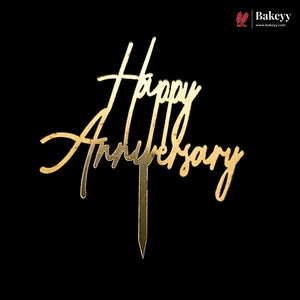 Gold metallic 'Happy Anniversary' script cake topper on a black background, with a Bakeyy logo in the top right corner.